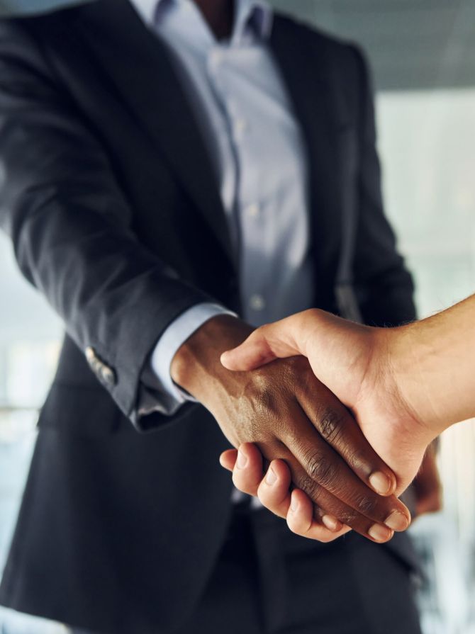 Doing handshake with customer. Young african american businessman in black suit is indoors.